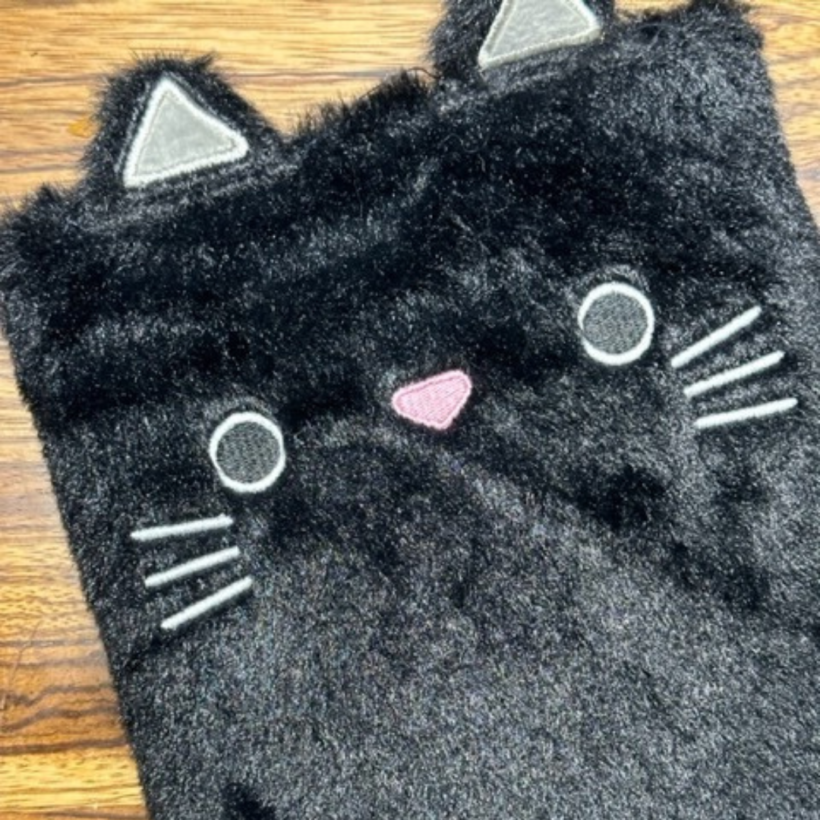 black fluffy notebook in the shape of a cat with ears, eyes nose and whiskers