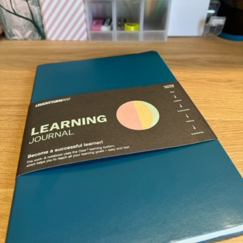 pacific green learning journal with belly band with the words "learning journal" on it sitting on desk