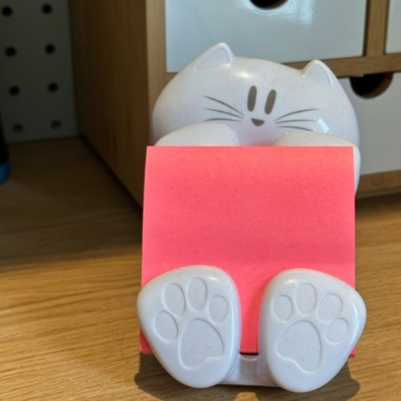 white cat shaped post it note dispenser with bright pink post it notes in it.