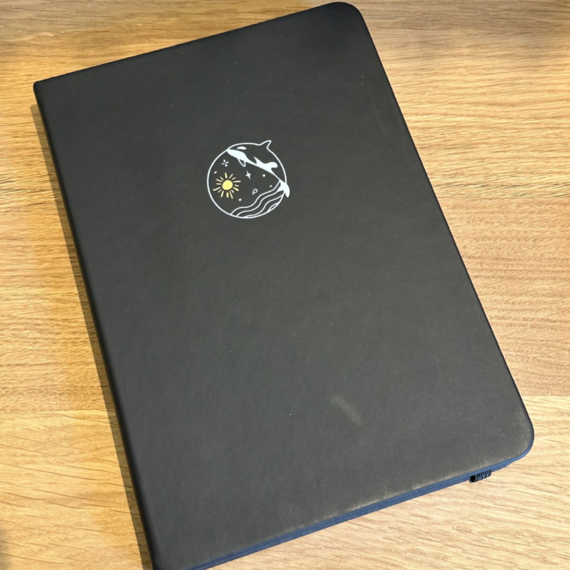 a5 notebook with black vegan leather cover and an orca on the front.