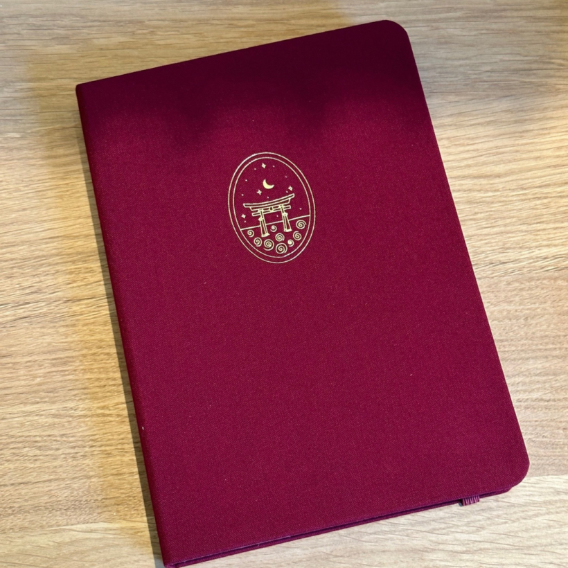 a5 notebook with a red linen cover with torii shrine on the front cover in gold.