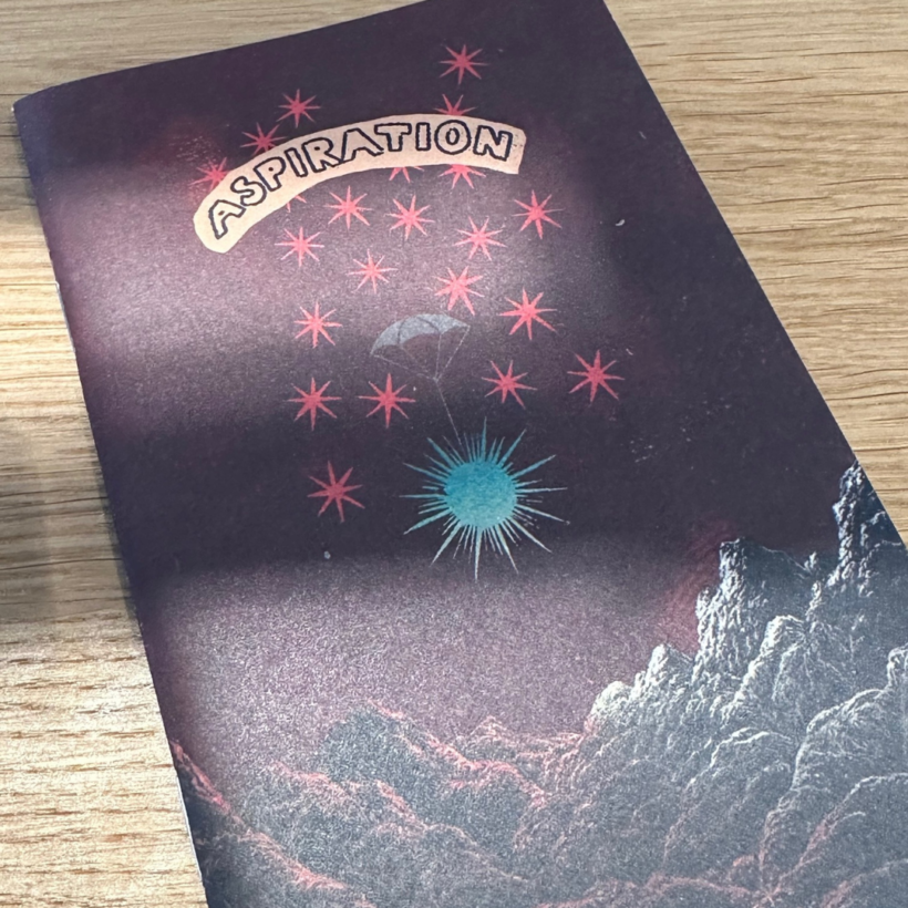 word pocket notebook with a dark red cover, with the work aspiration and stars over a rocky foreground on it.