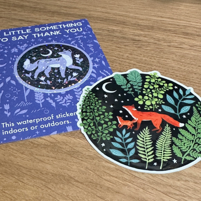 stickers from papio press, on features a fox in purple and black and the other has a fox and a cub in a green forest.