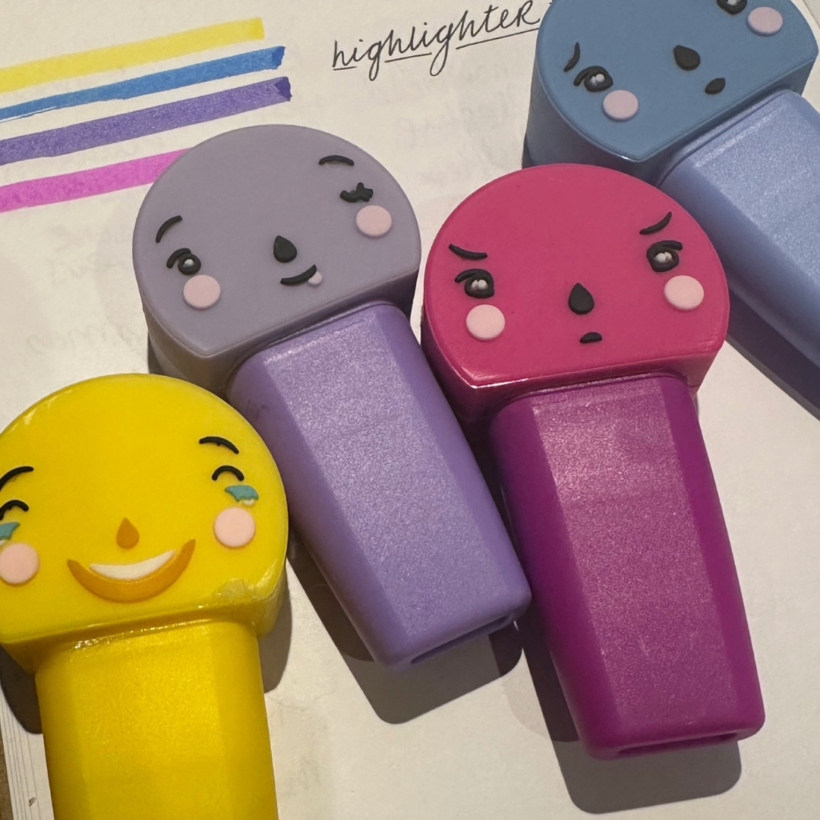 four highlighter pens in yellow purple, pink and blue on paper background with lines of the highlights