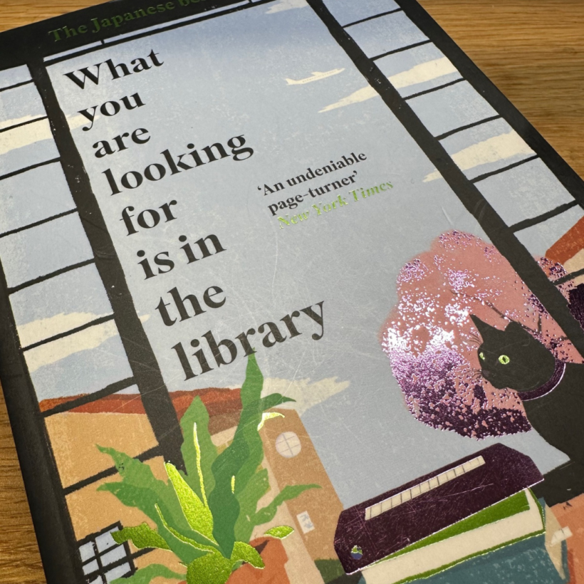 book with title what you are looking for is in a library on the cover with a picture of cat on windowsill on it.