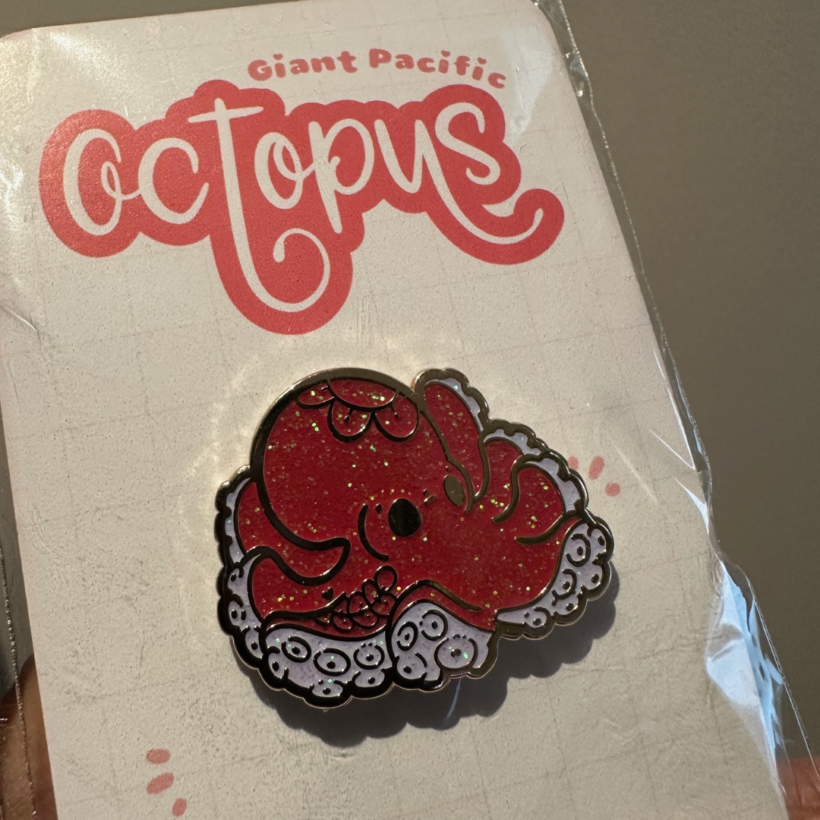 Giant Pacific Octopus enamel pin on backing card with the words Giant Pacific Octopus designed by evy benita