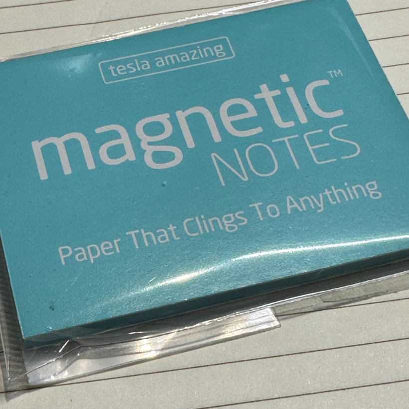 pack of aqua blue notesheets wrapped in packaging. The notes have white text on them which says tesla amazing magnetic notes paper that clings to anything.
